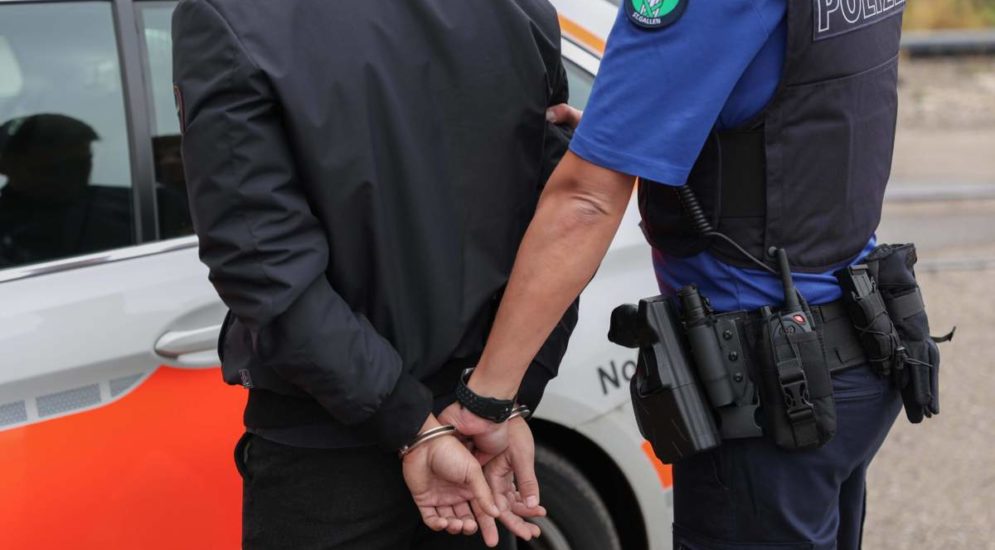 Mann in schwarzer Kleidung wird in Handschellen von Polizist zu Polizeiwagen geführt