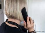 Person mit kinnlangen blonden Haaren schräg von hinten beim Telefonieren zu sehen, sie trägt eine schwarze Halskette und schwarzes Oberteil