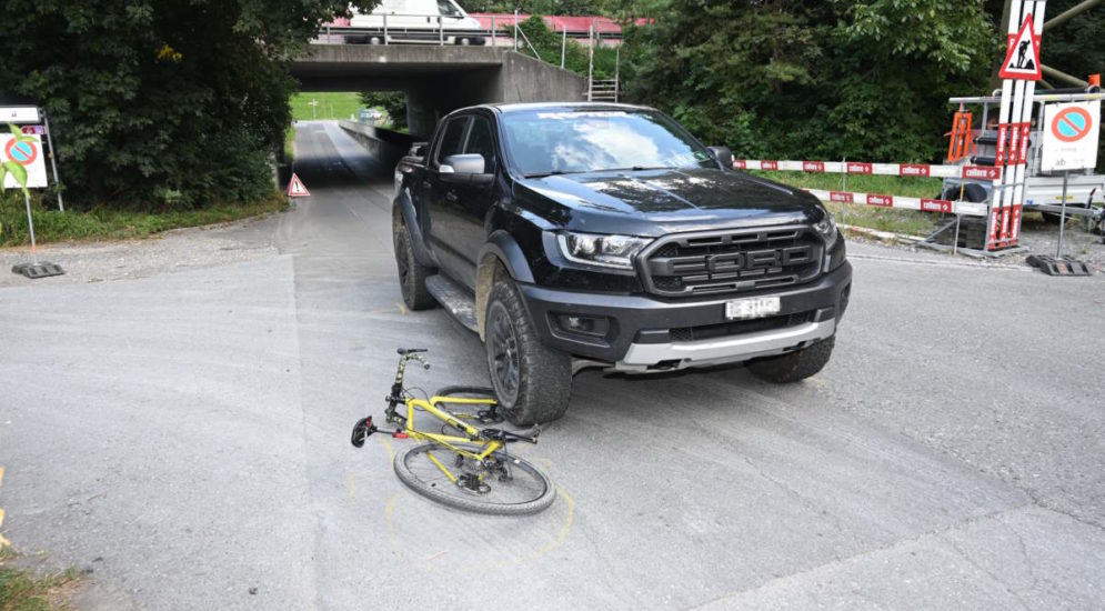 schwarzer Ford-Pickup steht mit dem Vorderreifen auf dem Vorderrad eines auf der Seiten liegenden gelben Rennrads