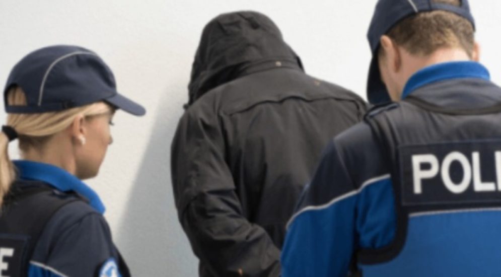 Symbolbild: einer Person in schwarzer Kapuzenjacke werden von zwei Polizeikräften Handschellen angelegt