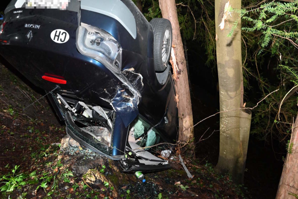 stark beschädigtes Unfallauto Renault Mégane auf dem Dach liegend neben zwei Bäumen