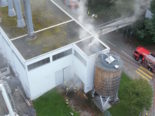 Luftbild: Rauch kommt aus Silo, einige Feuerwehrleute vor Heizzentrale