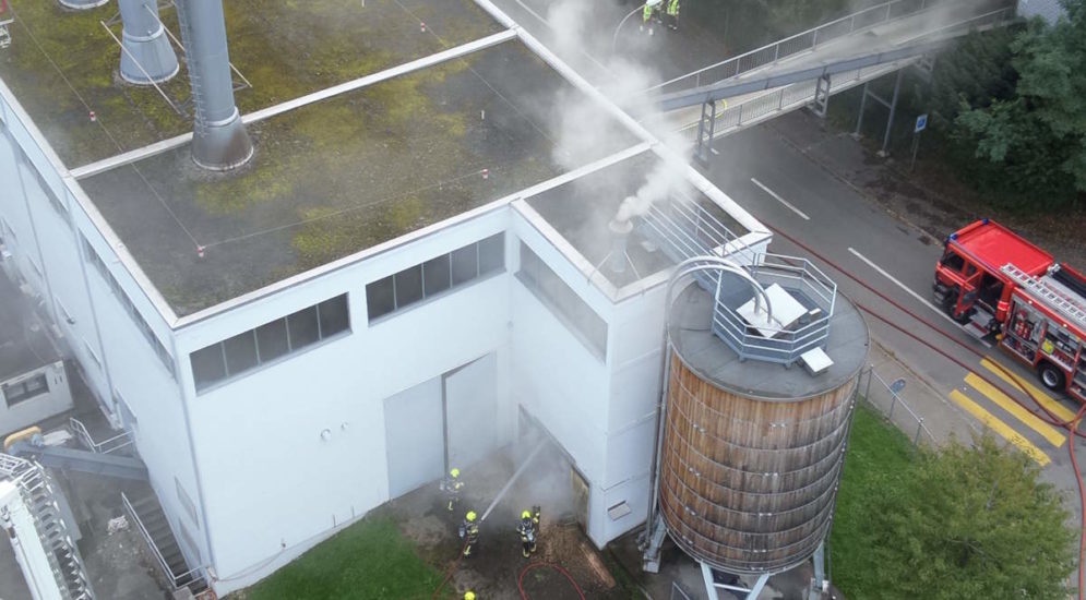 Luftbild: Rauch kommt aus Silo, einige Feuerwehrleute vor Heizzentrale