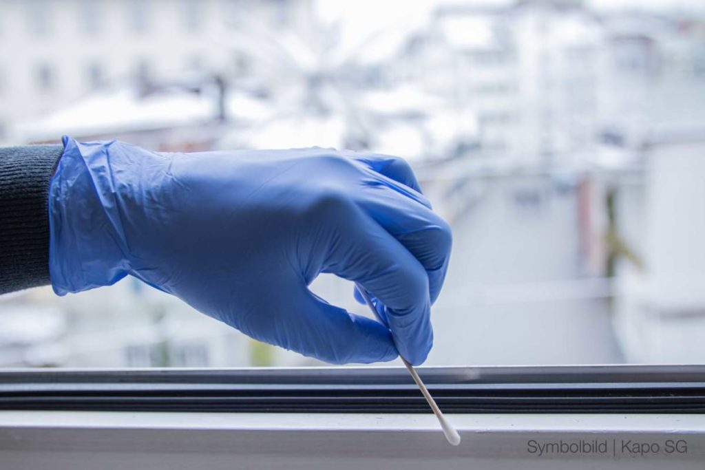 Symbolbild: Hand in einem blauen Gummihandschuh, die vor einem Fenster mit einem Wattestäbchen eine Probe nimmt