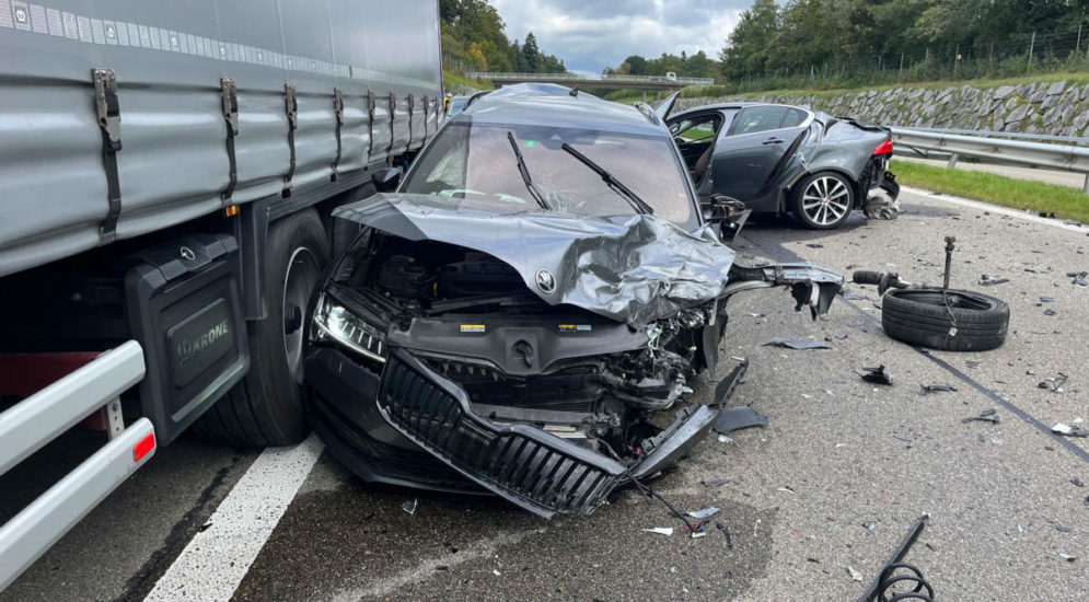 an der Front stark beschädigtes Auto neben Sattelschlepper, im Hintergrund ein weiteres Unfallauto