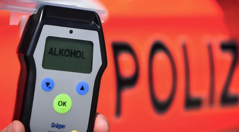 Symbolfoto: Alkoholmessgerät wird in der Hand gehalten, im Hintergrund ein Polizeiauto