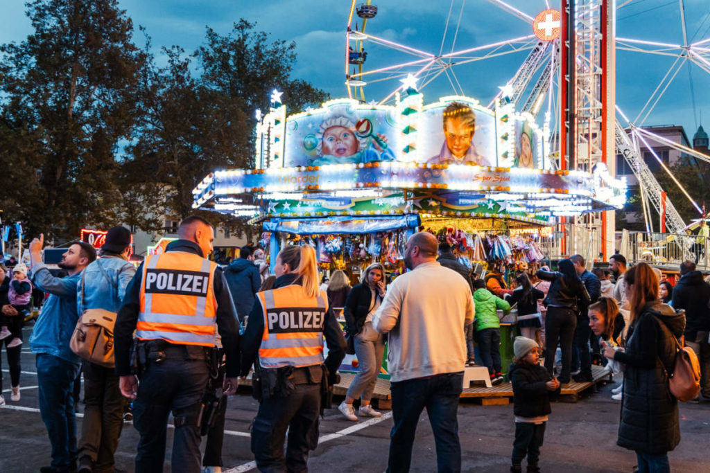 Zwei Polizist*innen stehen in einer Menschenmenge vor einem Fahrgeschäft