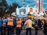 Zwei Polizist*innen stehen in einer Menschenmenge vor einem Fahrgeschäft