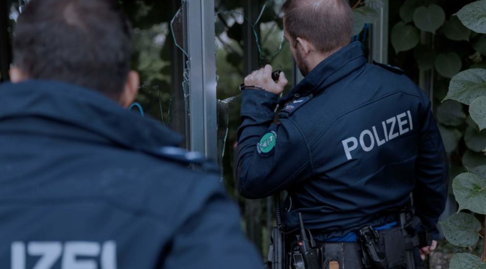 Symbolbild: Polizeibeamte leuchten durch zerbrochene Fensterscheiben