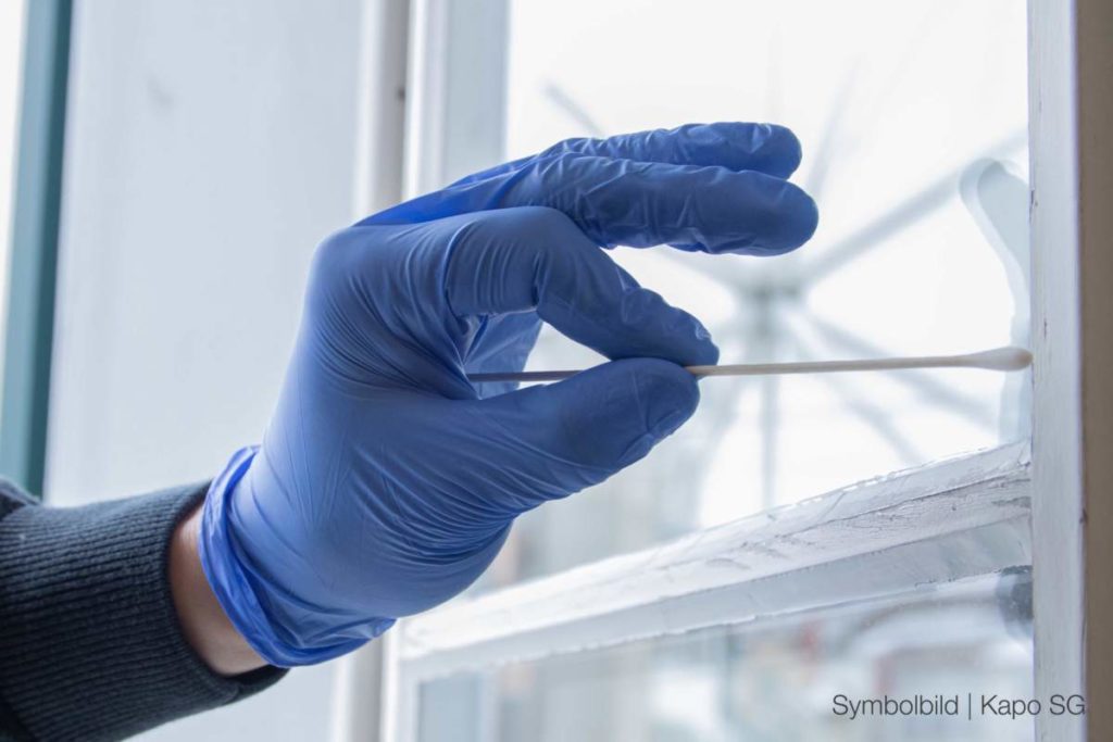 Symbolfoto: Hand in blauem Gummihandschuh nimmt mit Wattestäbchen eine Probe von einem Fenster