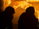 Symbolfoto: zwei als Silhouetten zu sehende Feuerwehrkräfte vor Feuerwand