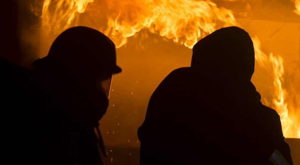 Symbolfoto: zwei als Silhouetten zu sehende Feuerwehrkräfte vor Feuerwand