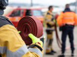 Symbolfoto: Feuerwehrkraft hält aufgerollten Schlauch in der Hand, im Hintergrund weitere Einsatzkräfte