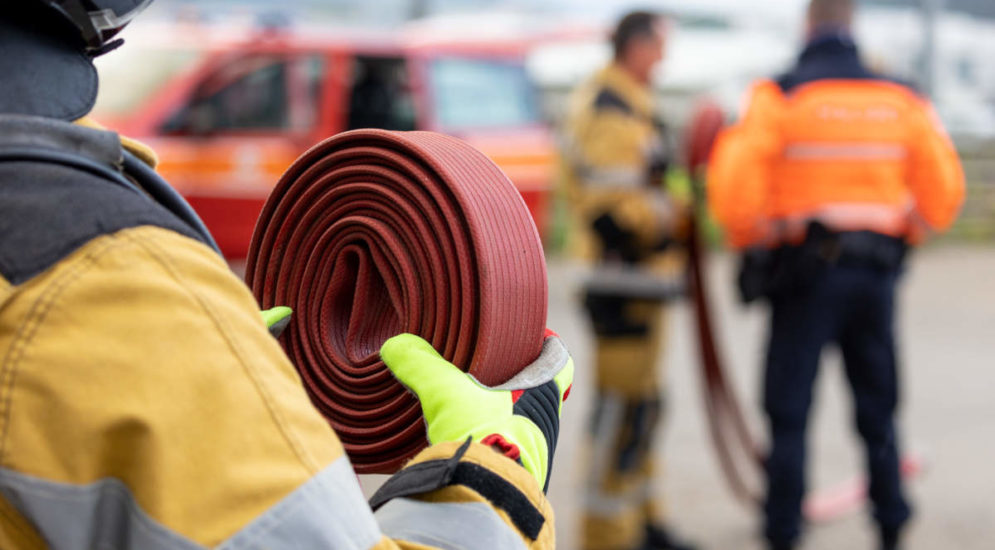 Symbolfoto: Feuerwehrkraft hält aufgerollten Schlauch in der Hand, im Hintergrund weitere Einsatzkräfte