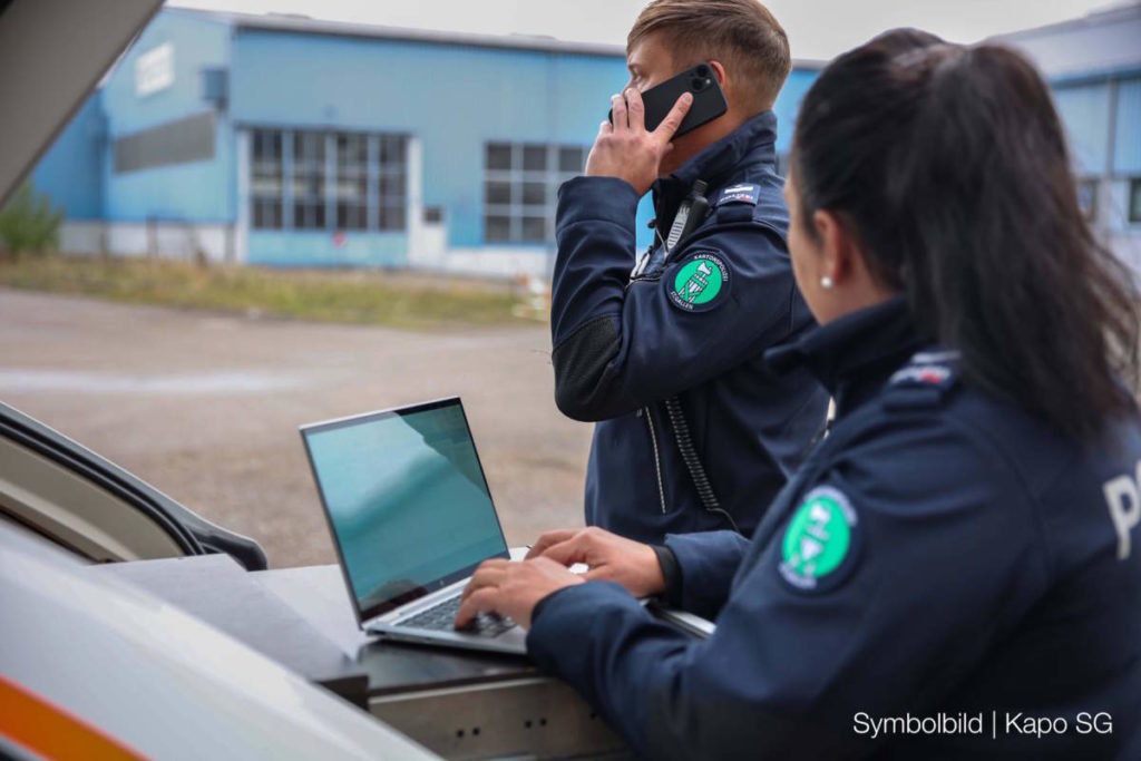 Symbolfoto: Zwei Polizist*innen im Ausseneinsatz, eine Person schreibt am Notebook, eine andere telefoniert