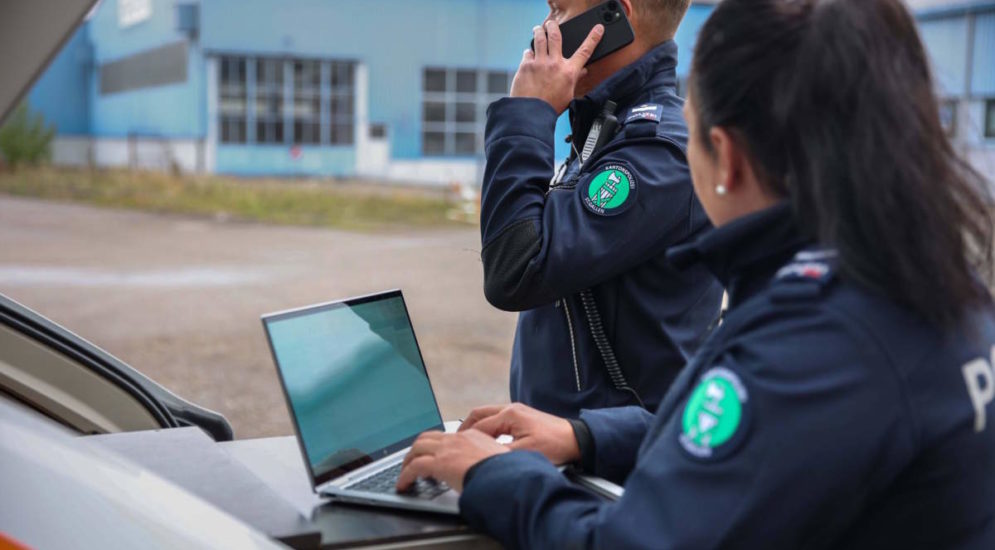 Symbolfoto: Zwei Polizist*innen im Ausseneinsatz, eine Person schreibt am Notebook, eine andere telefoniert